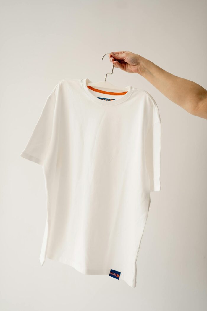 Clean white t-shirt on hanger held by human hand against a white studio background.